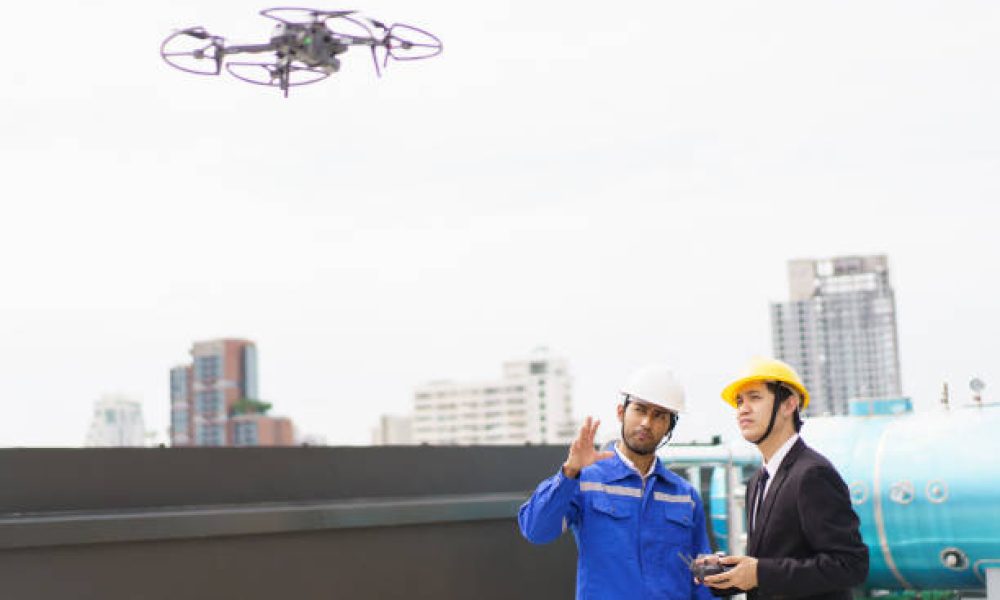 Professional Asian civil engineers using the unmanned aerial vehicle or UAV - drone for inspecting the building structure, 2 Asian foreman flying a drone to the building roof top area.